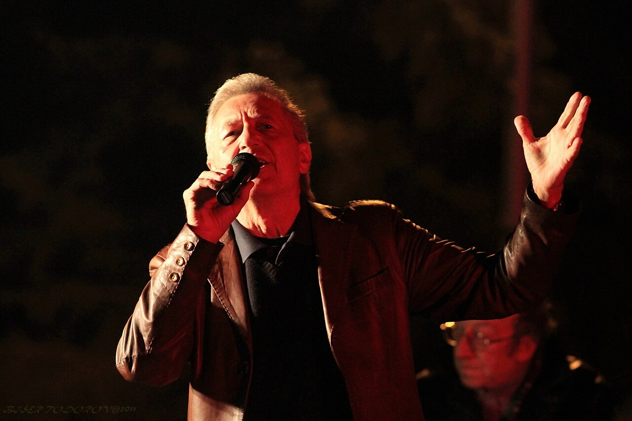 Miroslav Ilić singing on stage with a microphone under red concert lighting