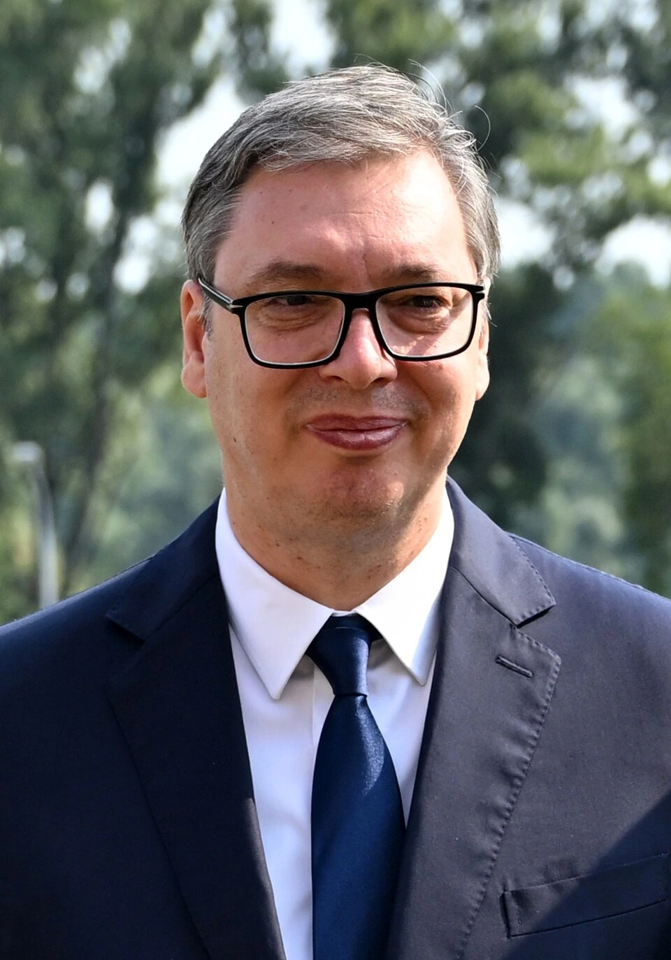 Aleksandar Vučić in a suit and glasses outdoors